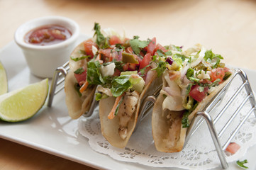 grilled chicken tacos on a metal stand with salsa and a lime wedge with lots of vegetables.