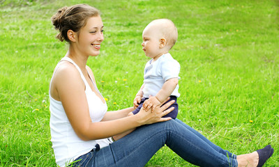 Naklejka na ściany i meble Happy smiling mother and son child sitting on the grass in summe