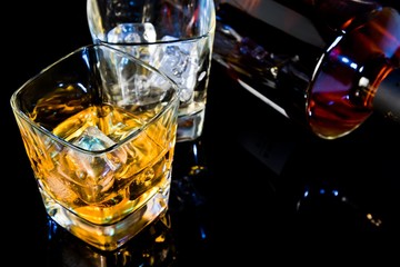 top of view of glass of whiskey near bottle on black table with reflection