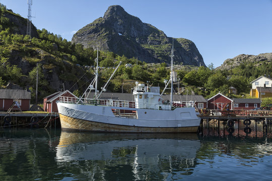 An old fishing boat in harbor with reflections in the water and mountains in the background