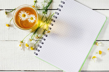A glass of herbal tea with chamomile and a note pad, a top view © elena_hramowa