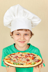 Young smiling boy in chefs hat with a cooked homemade pizza