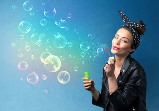 Pretty lady blowing colorful bubbles on blue background