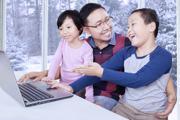 Cheerful boy showing laptop on his sister and dad