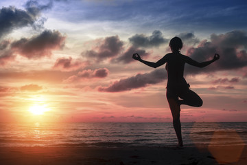 Fototapeta na wymiar Silhouette young woman practicing yoga on the sea beach at amazing bloody sunset.