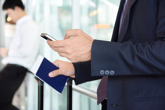 Businessman using smart phone while holding passport in another hand, at the airport