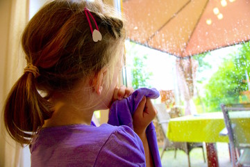 Kleines Mädchen am Fenster schaut nach Draußen in den Regen