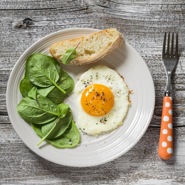 fried egg and fresh spinach on a white plate on a light wooden background, healthy Breakfast, snack