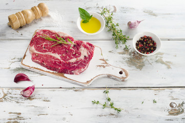 Raw ribeye steak on wooden cooting board.