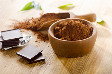 Chocolate bars with a wooden bowl of cacao powder.