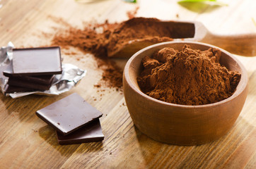 Chocolate bars with wooden bowl of cacao powder.