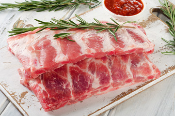 Raw ribs with sauces on wooden board.