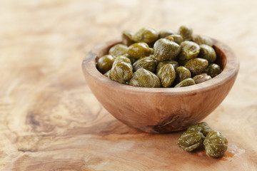 marinated capers in bowl on olive board