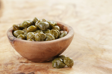 marinated capers in bowl on olive board