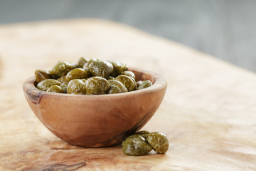 marinated capers in bowl on olive board