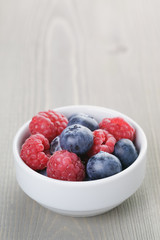 raspberries and blueberries in bowl on wood table