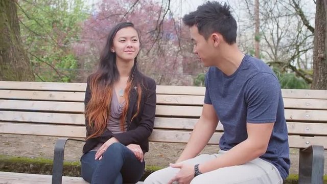 A young couple talking on a park bench