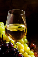 White wine in a glass and green and red grapes in a wicker baske