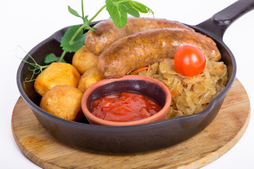 Grilled pork sausages with potato and red sauce in the bowl served in the pan on the wooden plate