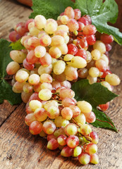 Pink grapes with green leaves on old wooden table, selective foc