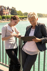 Zwei Geschäftsfrauen arbeiten draußen mit Smartphone und Table