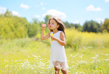 Child blowing soap bubbles on meadow in sunny summer day