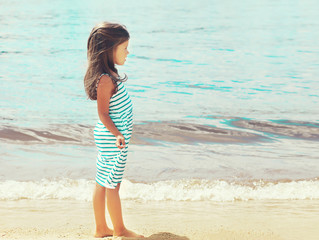 Fototapeta na wymiar Little girl child walks on the beach near sea in profile