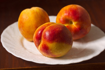 Fototapeta na wymiar Three ripe peaches on a plate.On a dark background.