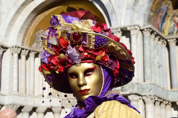Fototapeta na wymiar Intense look, golden mask with hat of different geometries in orange and violet tones during the Carnival of Venice, Italy