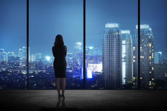 Woman standing in his office looking at the city at night