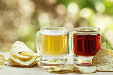Light and dark beer mugs in an old-fashioned potato chips on blu