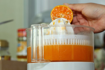 orange fruit squeezed with woman hand in juicer machine