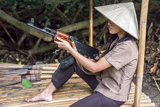 woman with a machine gun sits in a bamboo shelter