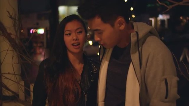 A young couple talking on a city sidewalk at night