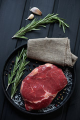 Frying pan with raw ribeye beefsteak and seasonings, top view