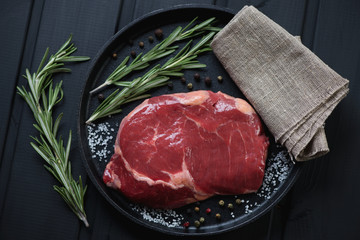 Above view of raw ribeye steak with salt, pepper and rosemary