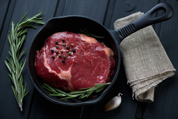 Raw steak ribeye with seasonings in a frying pan, above view