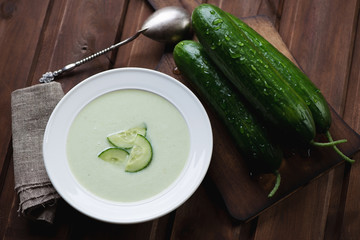 Cucumber soup and fresh cucumbers over rustic wooden surface