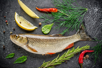 Fresh fish ide on a black stone slab surrounded by herbs, slices of lemon