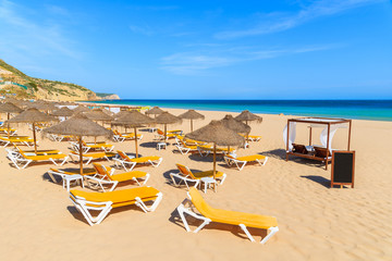 Umbrellas with sunbeds on golden sand beach in Salema town, Portugal