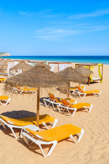 Umbrellas with sunbeds on golden sand beach in Salema town, Portugal