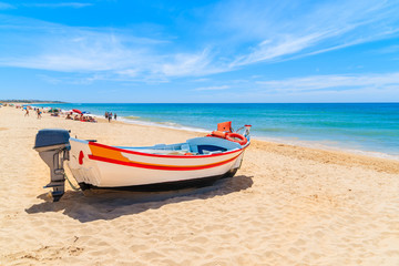 Fototapeta na wymiar Typical colourful fishing boat on sandy beach in Armacao de Pera village, Algarve region, Portugal