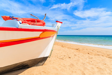 Naklejka premium Traditional colourful fishing boat on sandy beach in Armacao de Pera village, Algarve region, Portugal