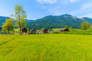Fototapeta na wymiar Green meadow in small alpine village on shore of Weissensee lake with traditional boat houses in background, Austria