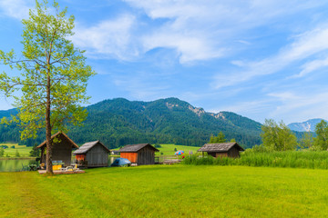 Fototapeta na wymiar Green meadow in small alpine village on shore of Weissensee lake with traditional boat houses in background, Austria