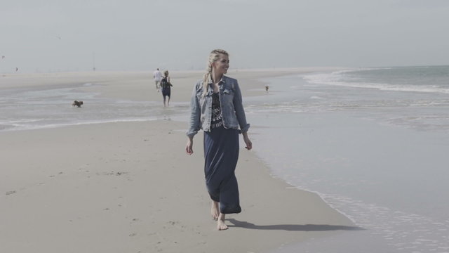 Portrait of young woman walking on beach with arms outspread and face raised in sky enjoying peace.