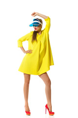 Like A Doll. Fashion model posing in red high heels, yellow mini dress and blue plastic sun visor. Full length studio shot isolated on white.