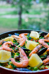 Close up fresh juicy prepared classic spanish dish paella with seafood, blueshell mussels, shrimps, rice with saffron spice, vegetables, smoked sausages and peaces of lemon with parsley in frying pan