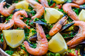 Close up fresh juicy prepared classic spanish dish paella with seafood, blueshell mussels, shrimps, rice with saffron spice, vegetables, smoked sausages and peaces of lemon with parsley in frying pan