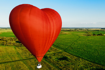 Red balloon in the form of heart over green fields and forests